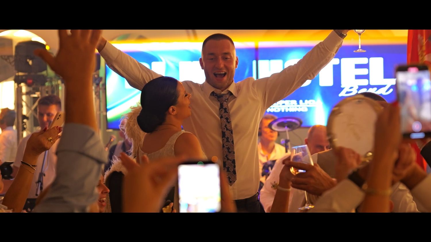 A large group celebrate with raised arms in a crowded indoor venue.