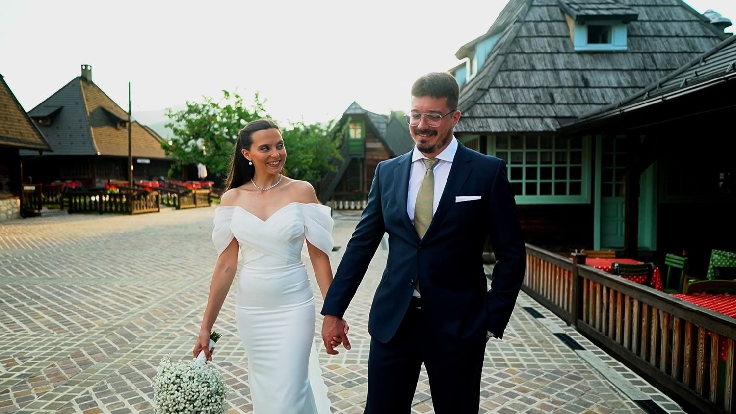 Newlyweds walking together outside a rustic building with green shingled roof.