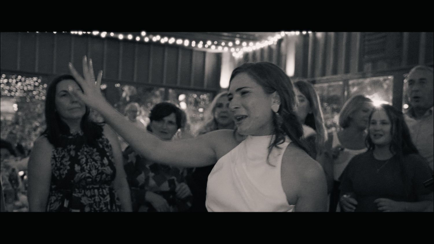 Joyful dancing and celebration at a wedding reception with string lights overhead.