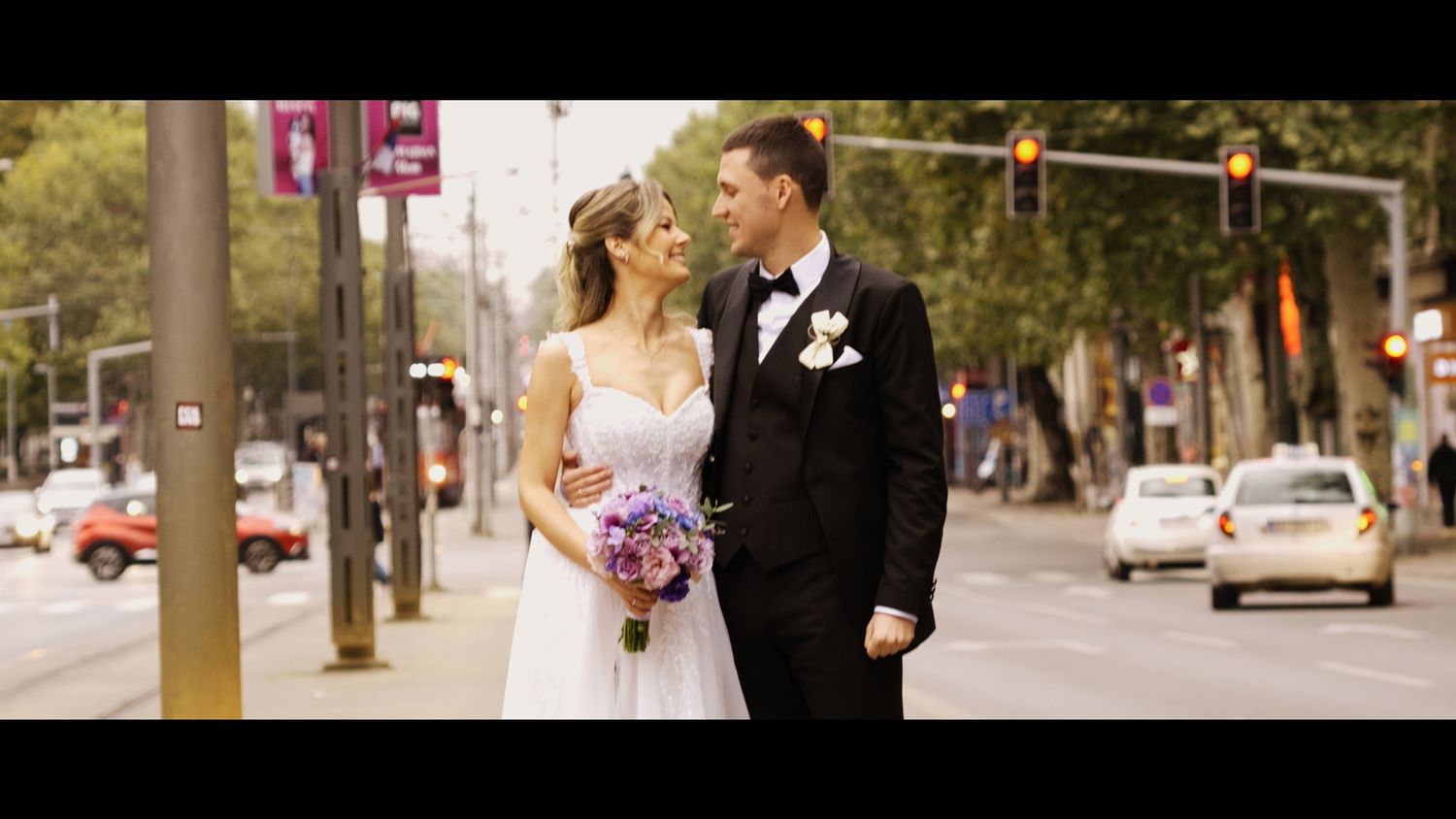 Wedding couple walking together on a tree-lined urban street.