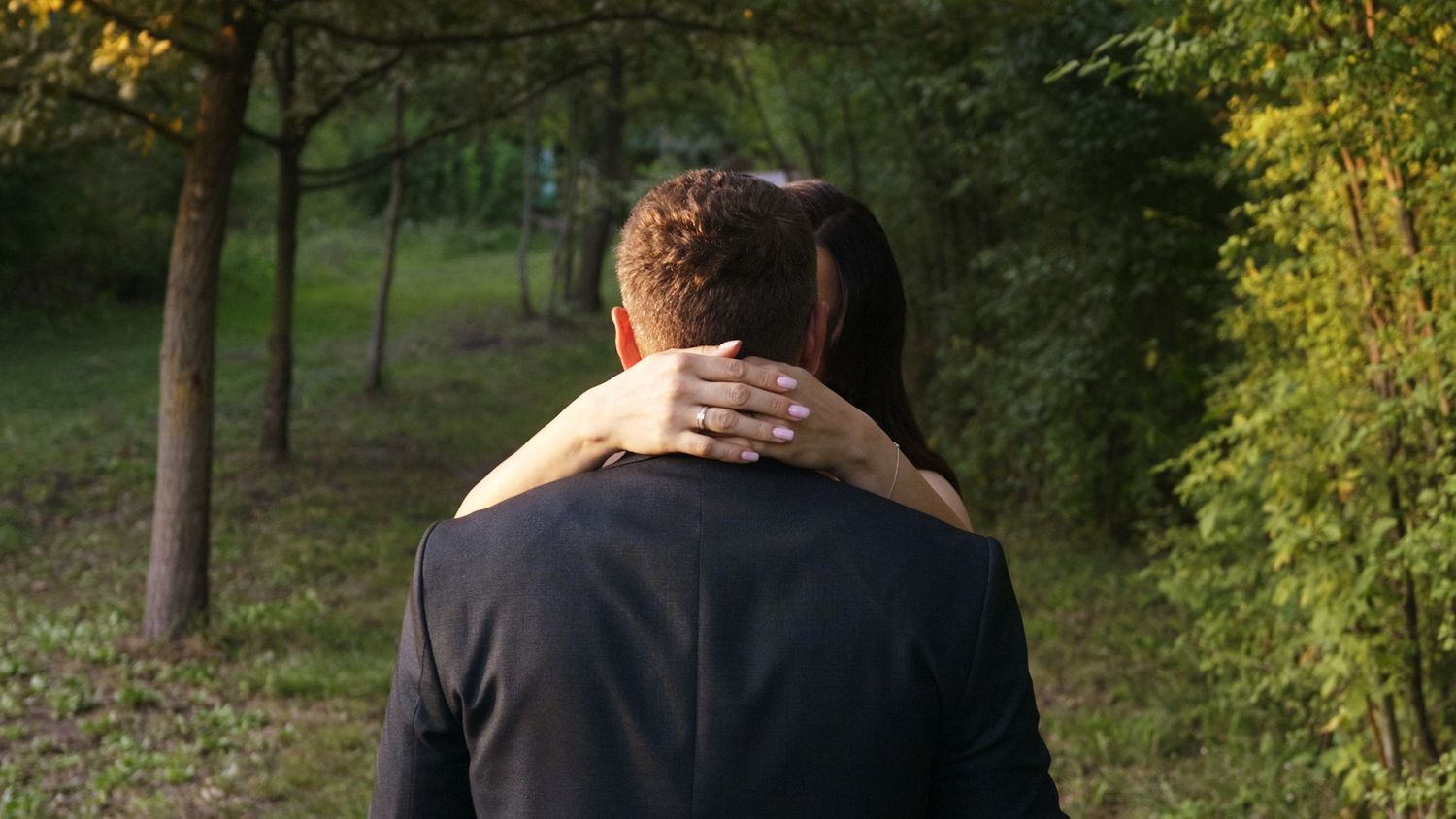 Wedding couple embracing in wooded setting with natural green backdrop.