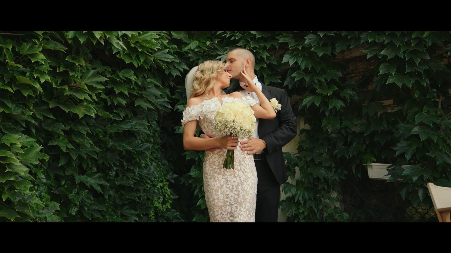 Intimate wedding moment captured in garden setting with lush green foliage.