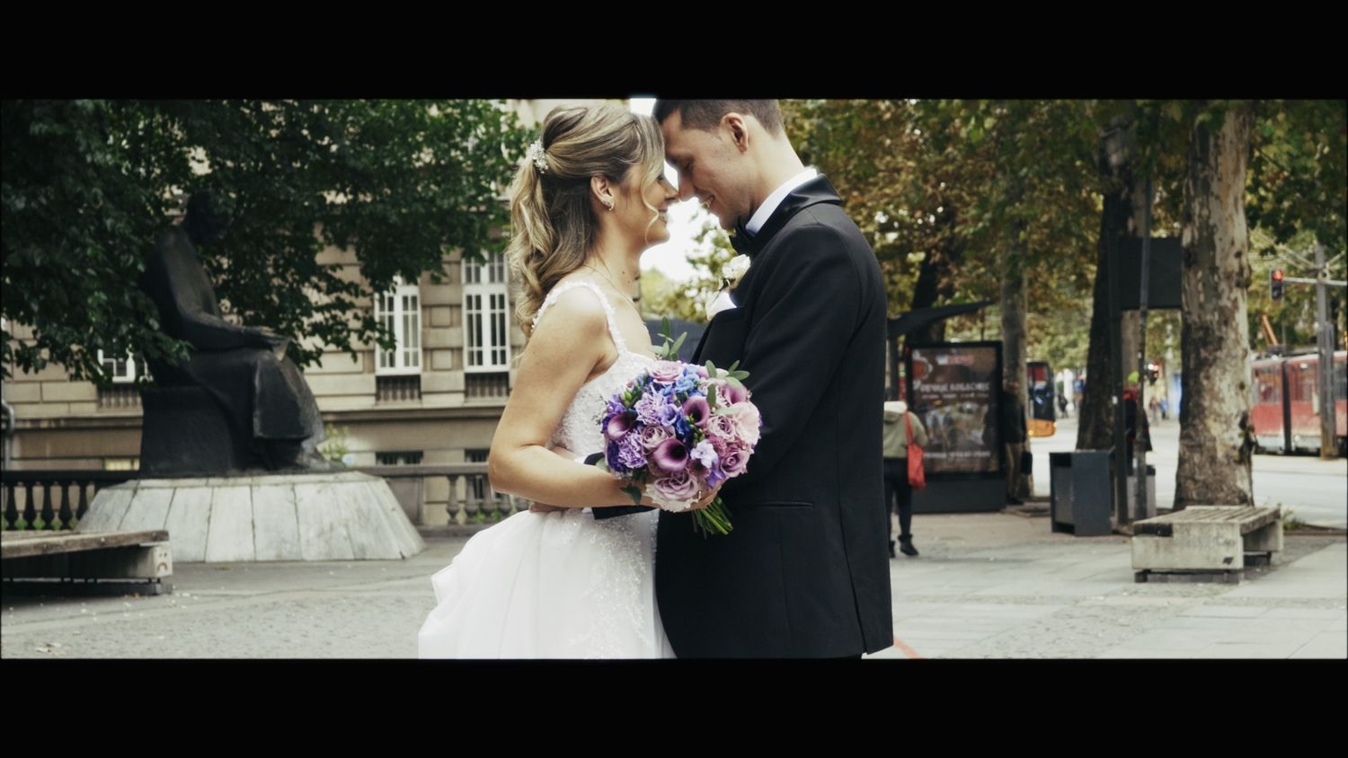 Couple embraces while holding a purple bouquet during their outdoor wedding ceremony.