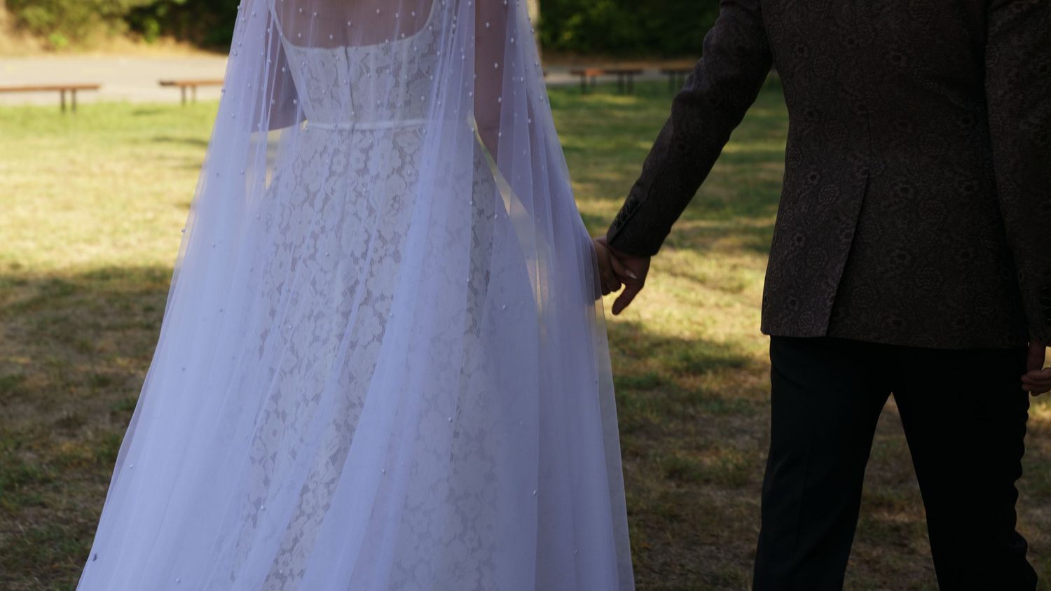 White wedding dress details with flowing veil against natural outdoor backdrop.