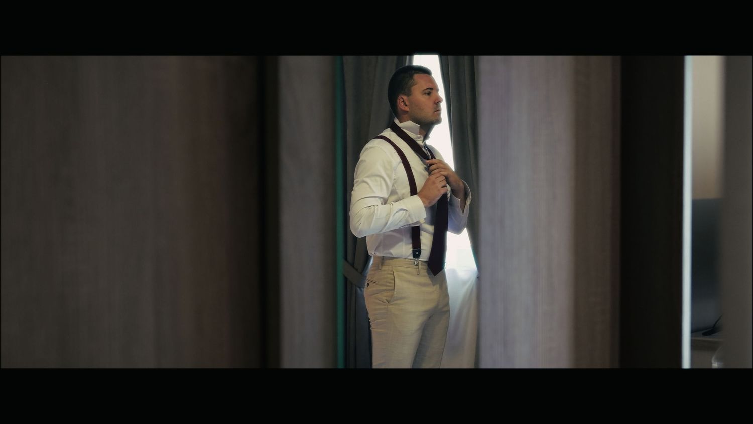 Person in light colored suit adjusting tie in hallway.