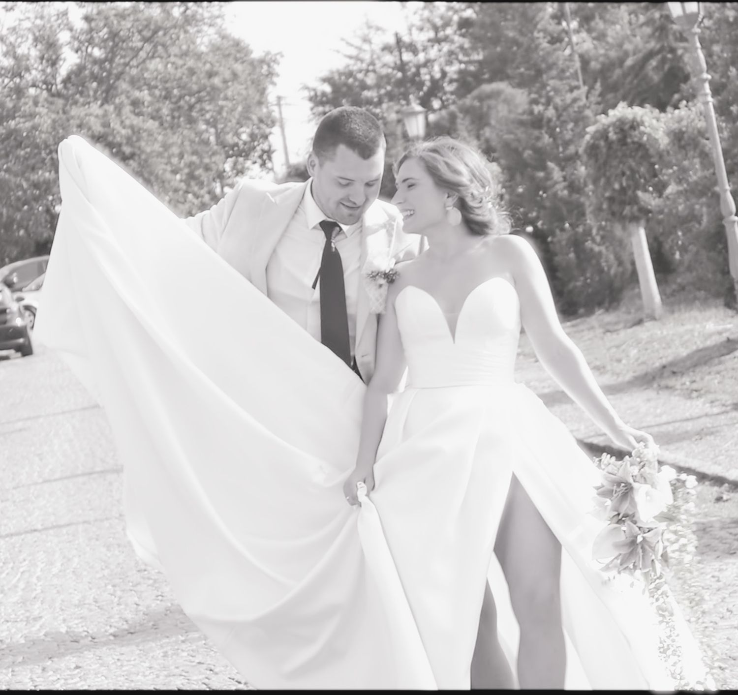 Bride in flowing white dress twirls playfully outdoors during a wedding photo session in a natural setting.
