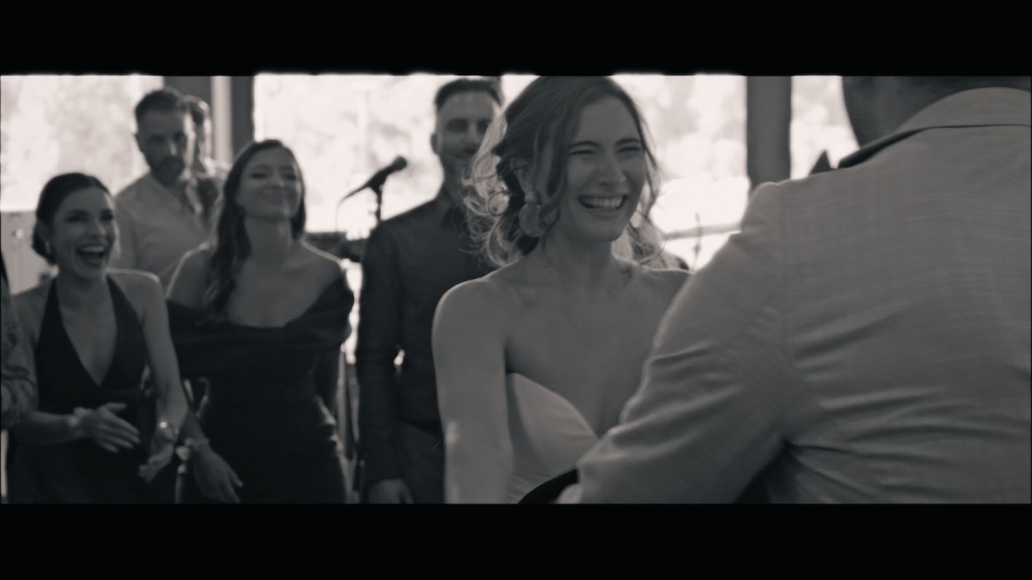 A candid black and white moment during a wedding ceremony with guests in the background.
