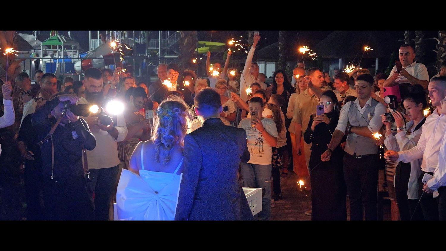 Wedding reception guests dancing and celebrating on a dimly lit dance floor with sparklers.