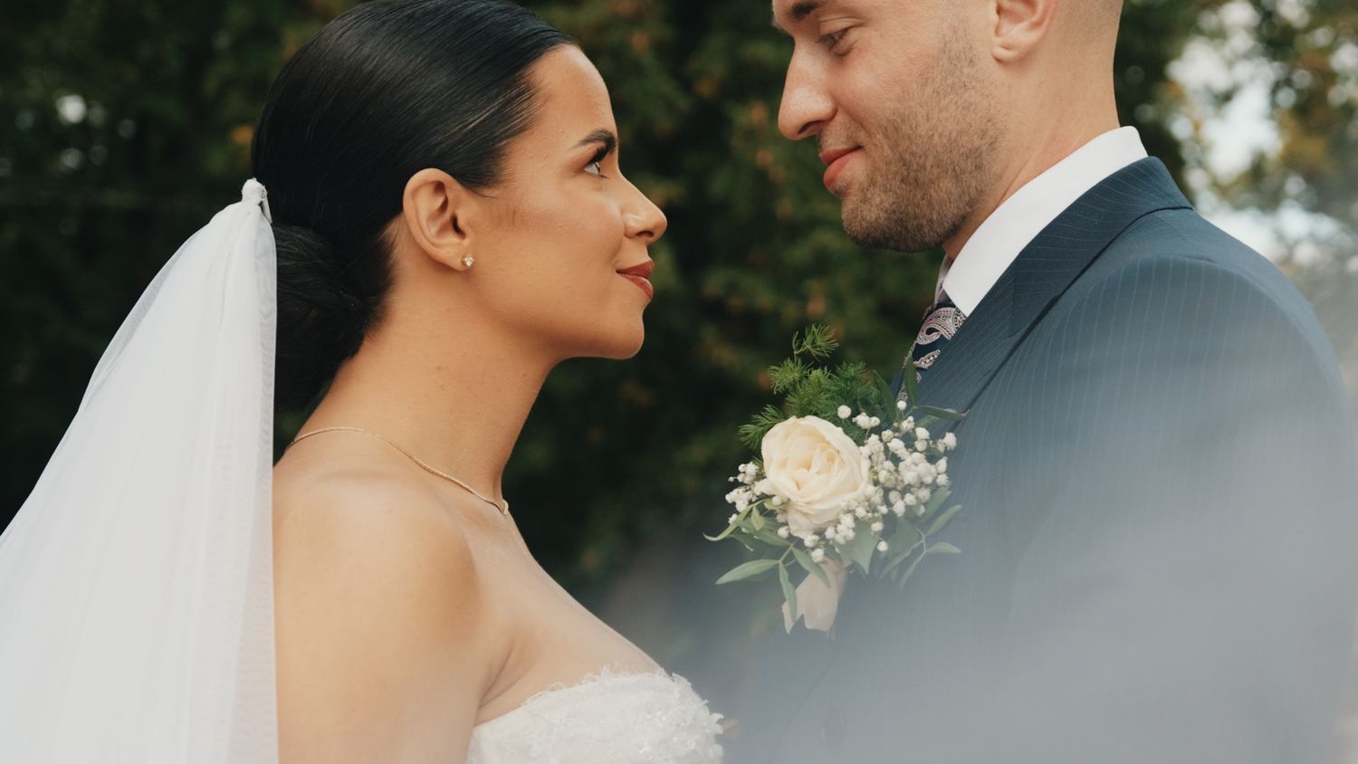 Close-up of newlyweds sharing a tender moment outdoors with bride wearing a white veil.