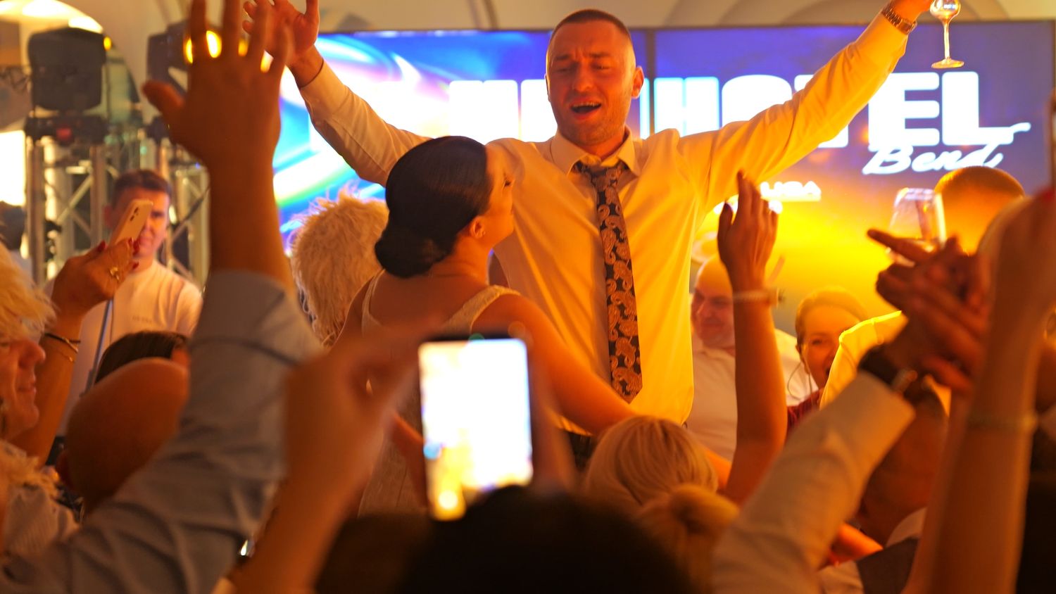 Wedding celebration reaches peak excitement as guests dance and celebrate on a crowded dance floor.