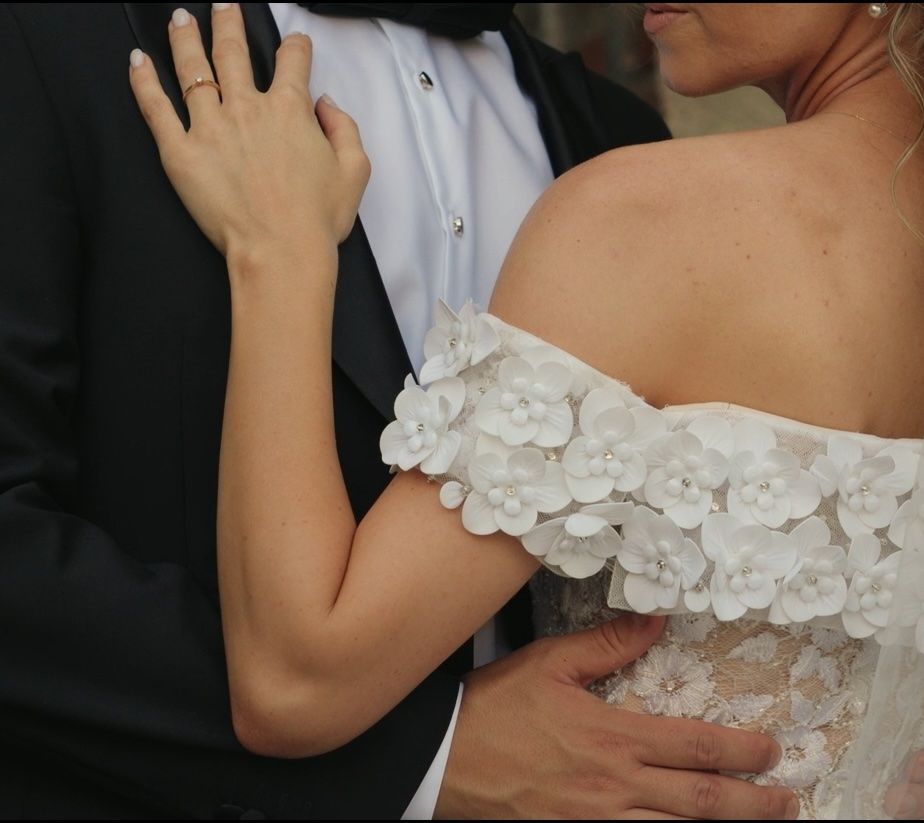 Close-up of bride's lace detailed dress sleeve and groom's formal attire.