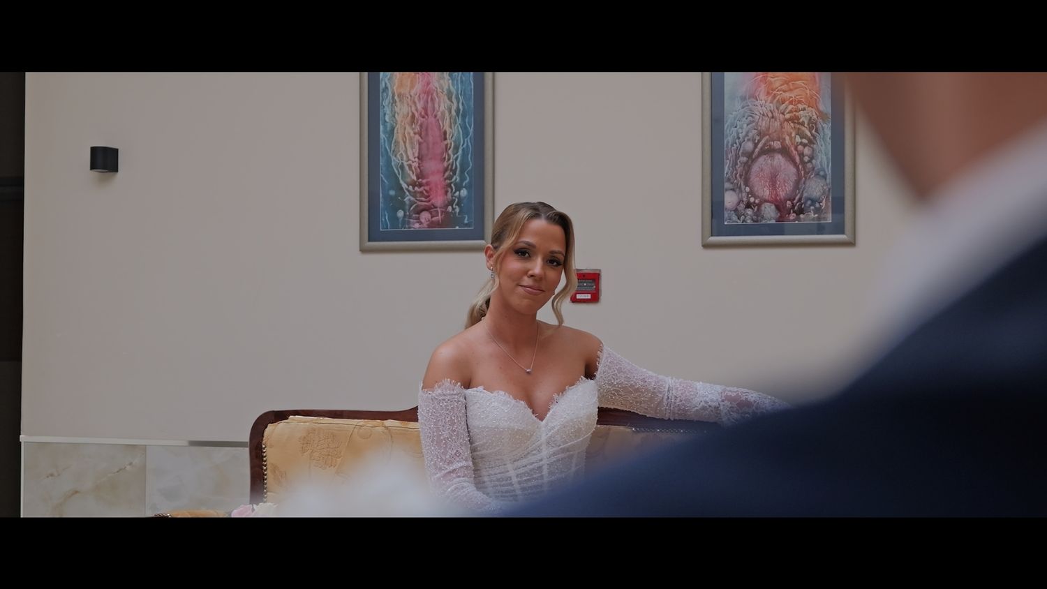 Elegant bride in lace dress holding pink bouquet while standing in an indoor venue.