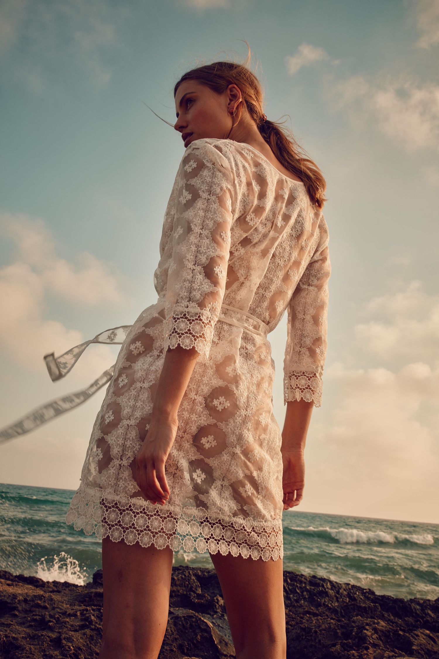 White lace beach dress photographed against dramatic ocean landscape.