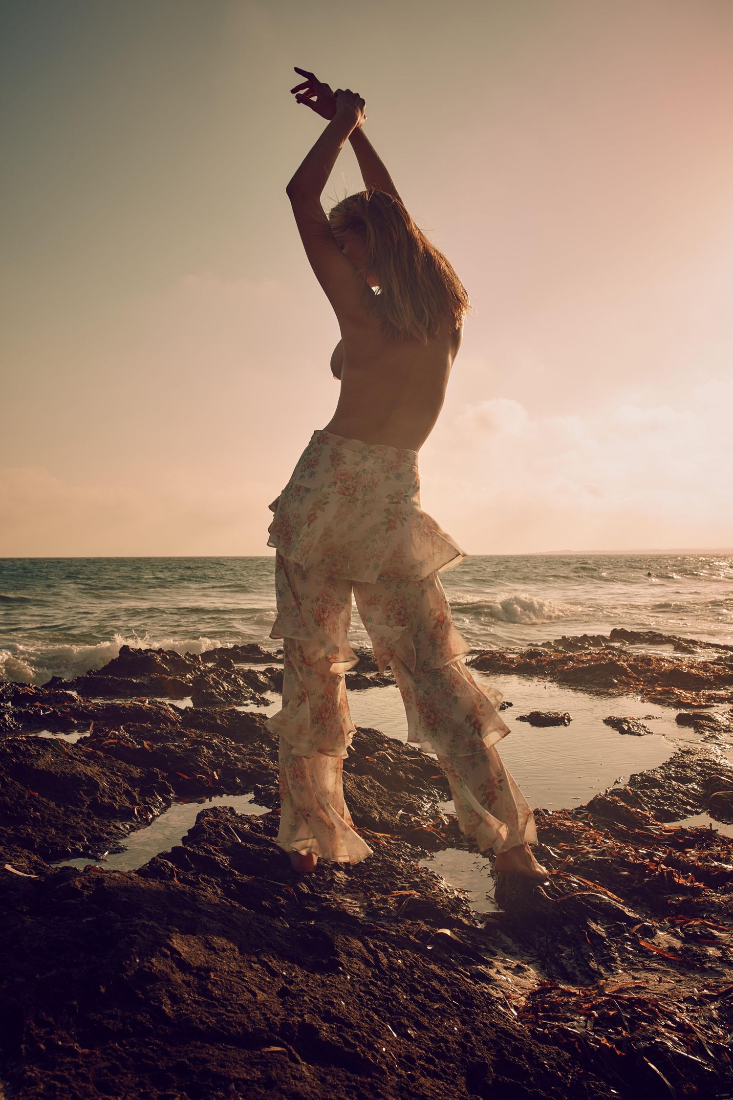 Dramatic silhouette dances on coastal rocks at sunset with waves crashing behind.