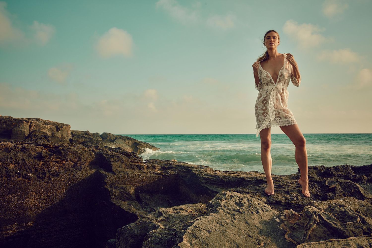Silhouette stands confidently on rocky beach outcrop against turquoise ocean and sky.