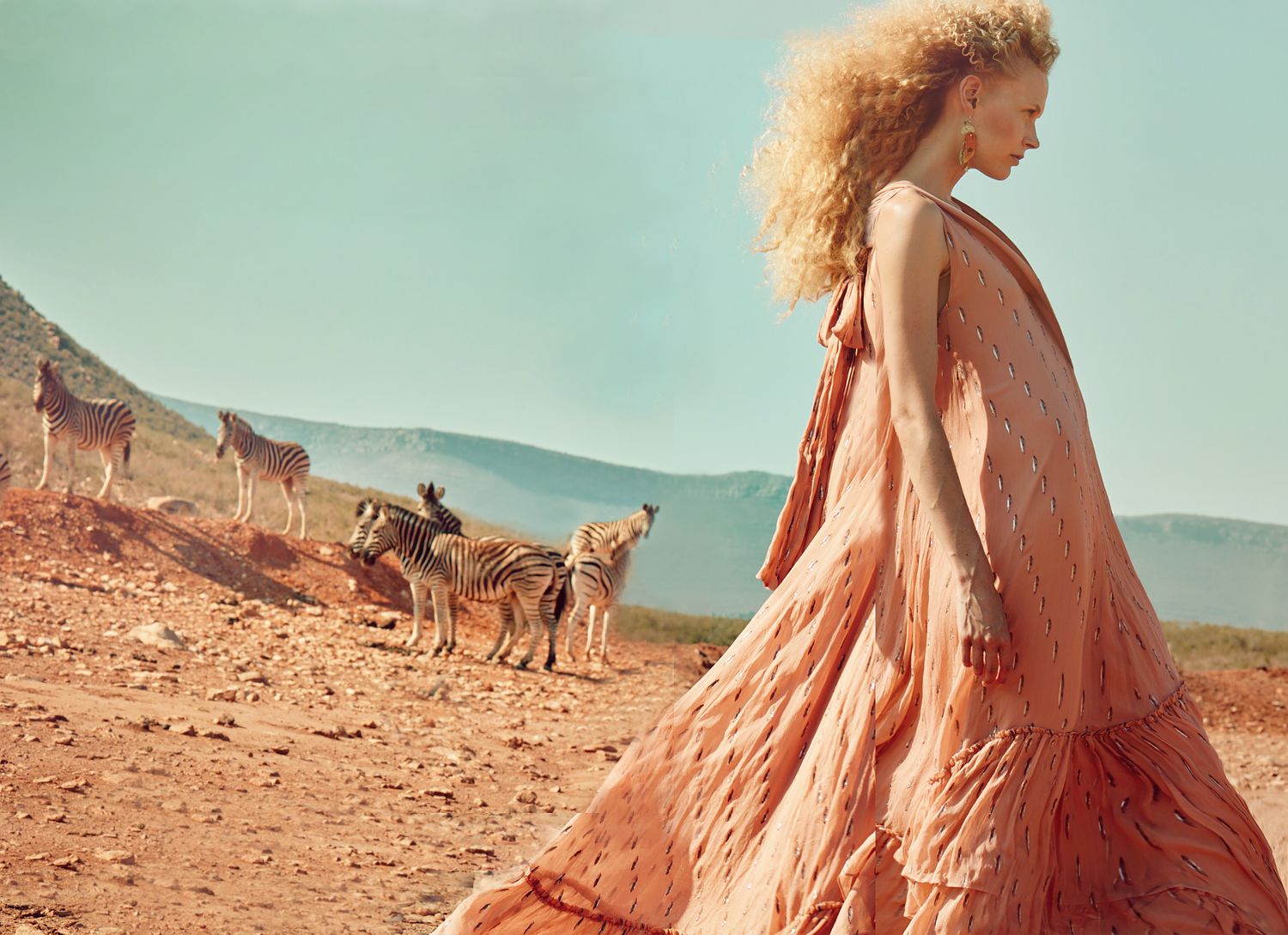 Desert photoshoot featuring flowing pink dress and horses in distant background.
