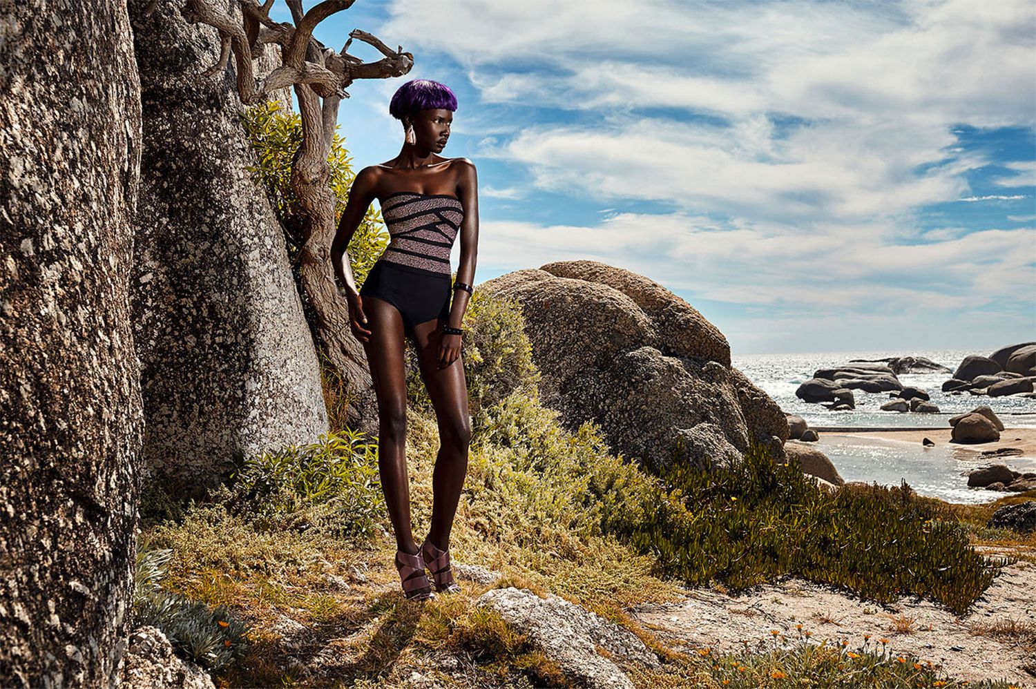 Coastal photoshoot on rocky terrain with blue sky and ocean backdrop.