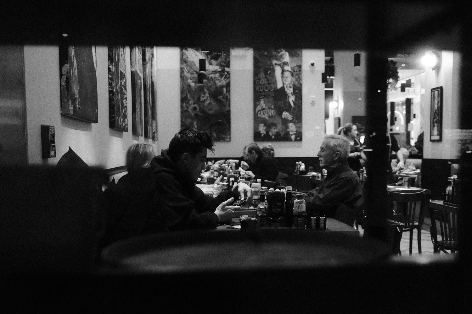 People seated at tables inside a restaurant, viewed through a gap with artwork on the walls.