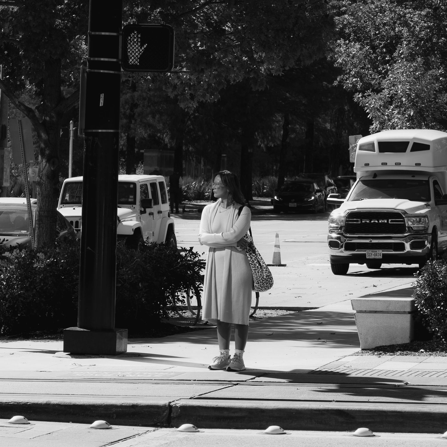 Woman standing at a crosswalk with her arms crossed while vehicles wait behind her.