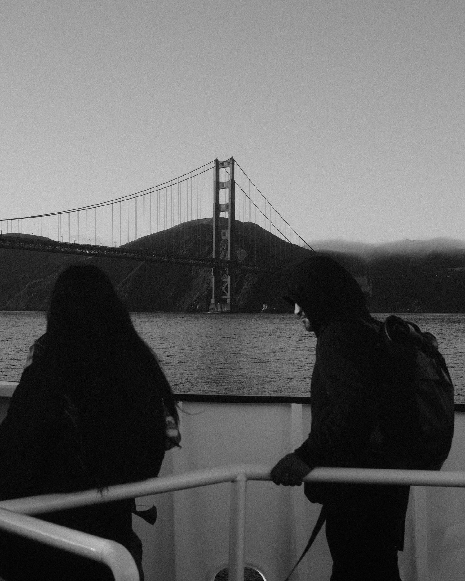 Two people standing on a boat deck with the Golden Gate Bridge visible across the water.