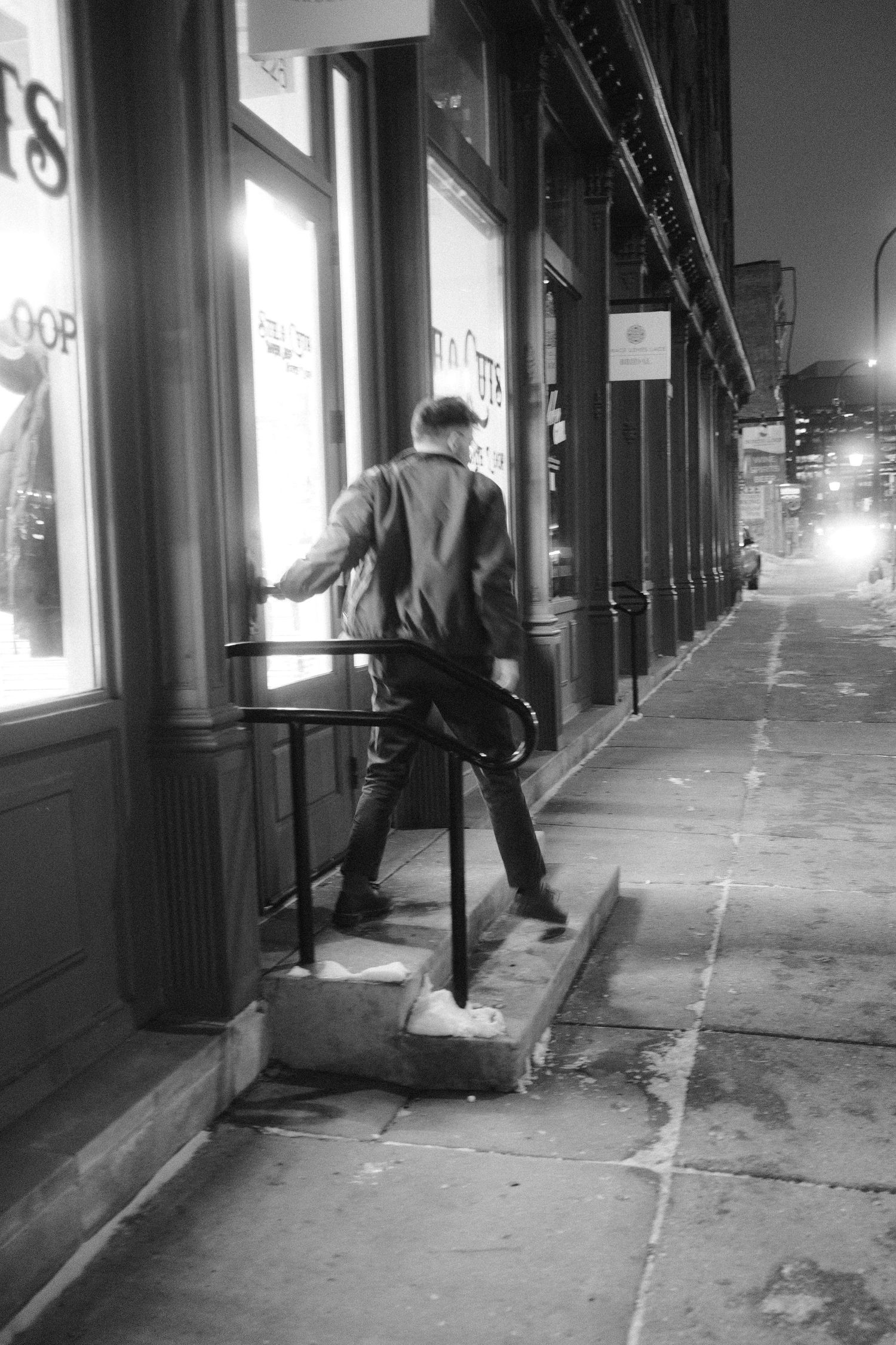 Man stepping up to open a door along a city sidewalk at night.