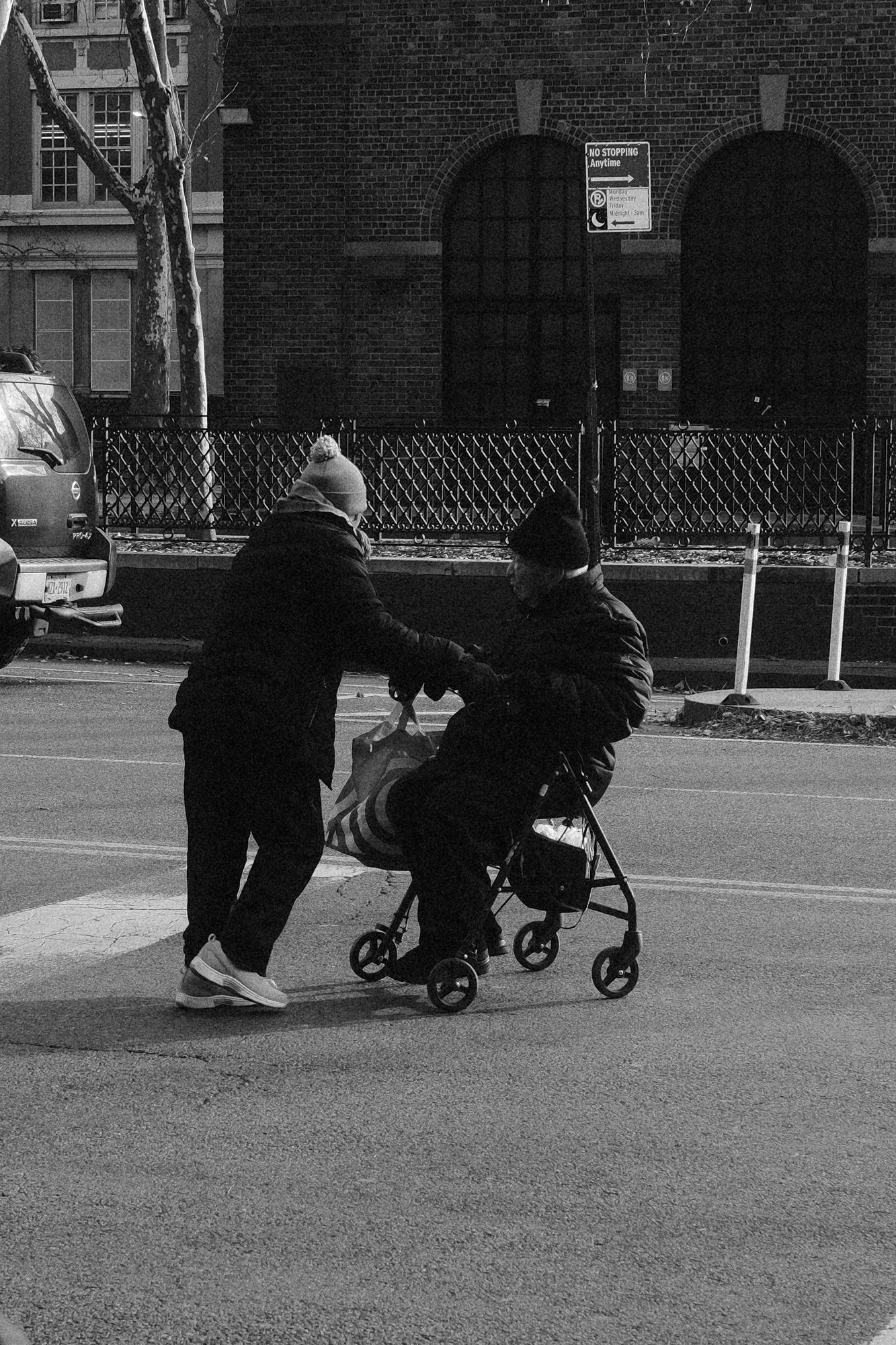 Person helping an individual seated in a walker chair while crossing a street.