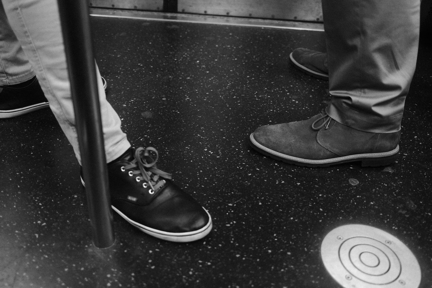 Close-up of two people’s shoes standing on a subway train floor.
