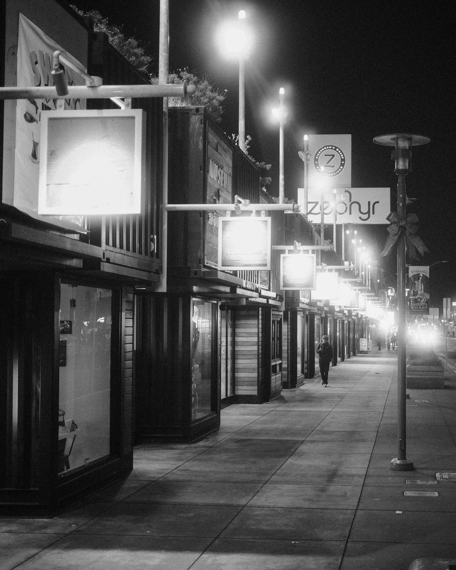 Row of illuminated storefront signs lining a city sidewalk at night.