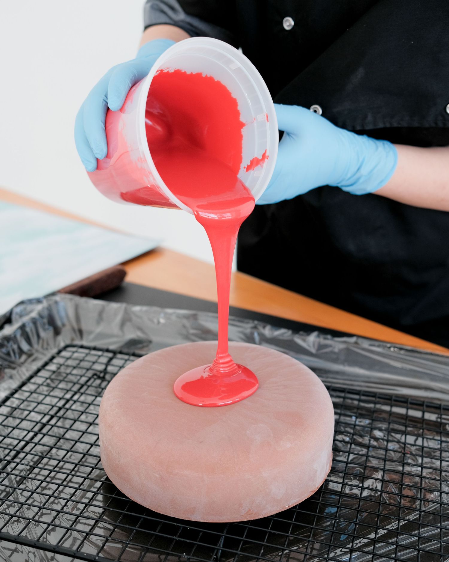 Hands in blue gloves pouring bright red liquid onto a circular mold.