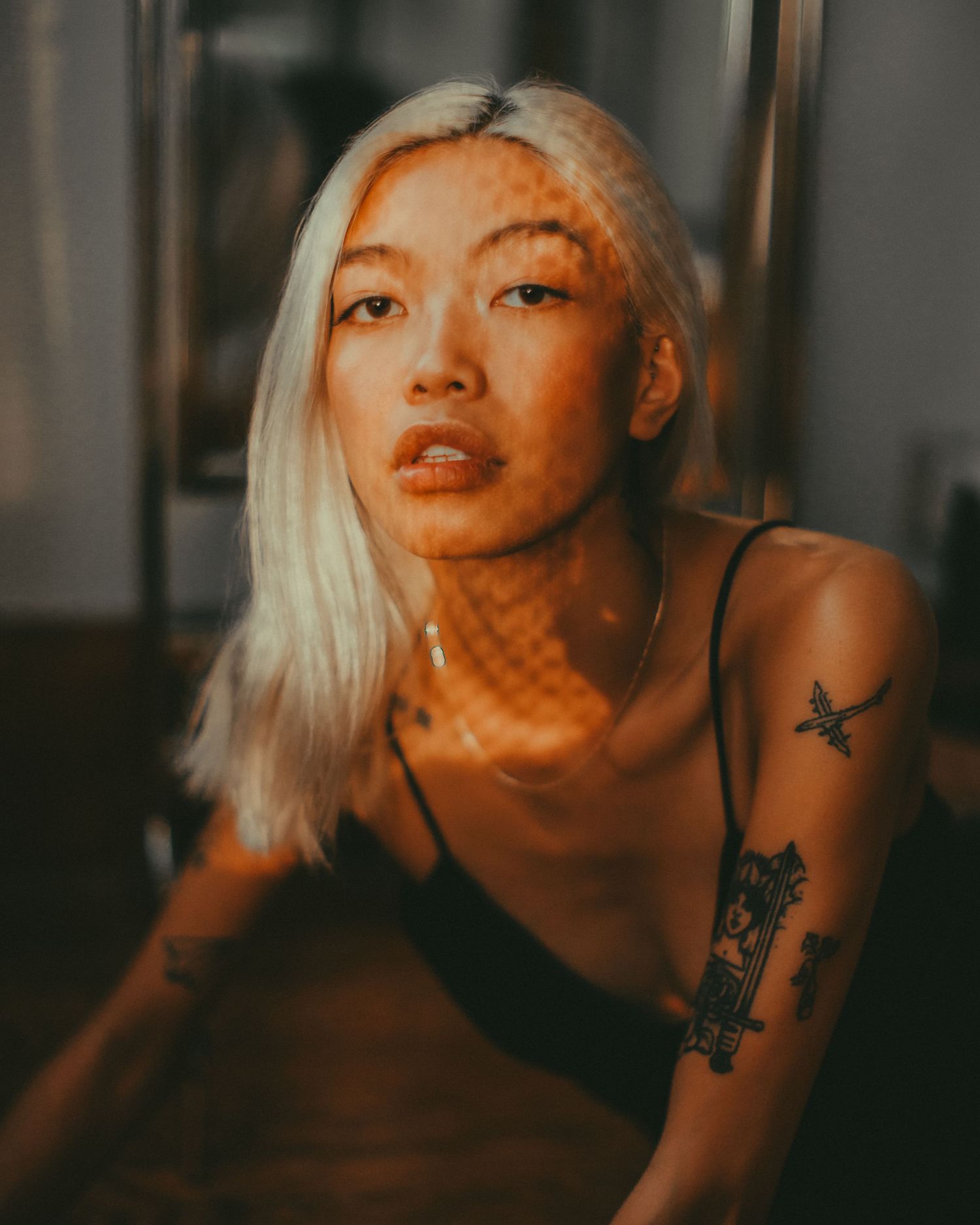 Artistic portrait with warm lighting showcasing platinum blonde hair and arm tattoos.