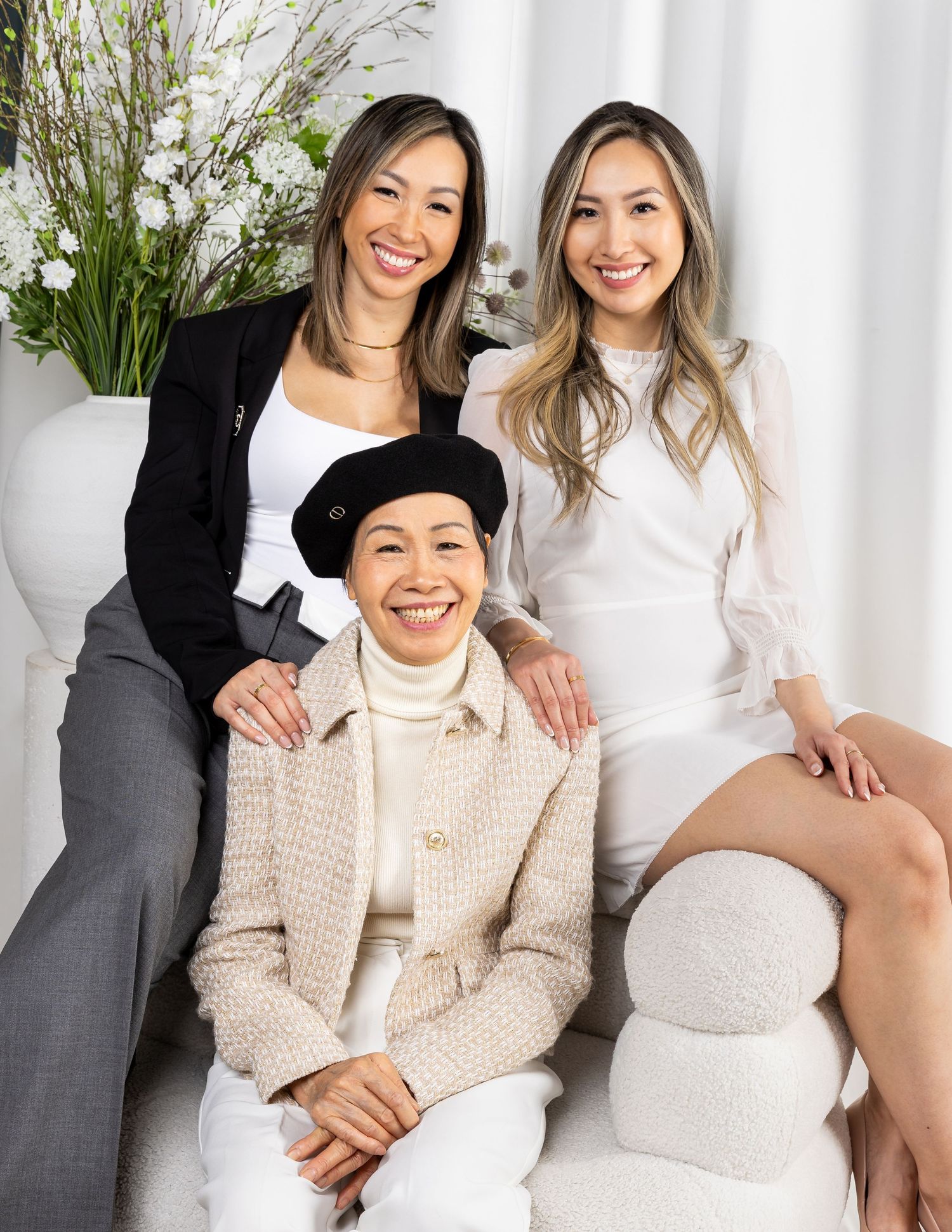 Professional studio photoshoot featuring casual and elegant poses on a white couch with indoor plants in background.