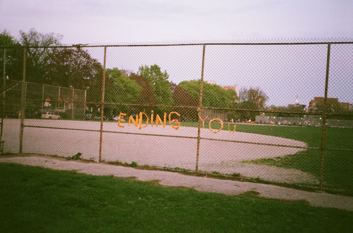 Empty baseball field with chain link fence and distant buildings.