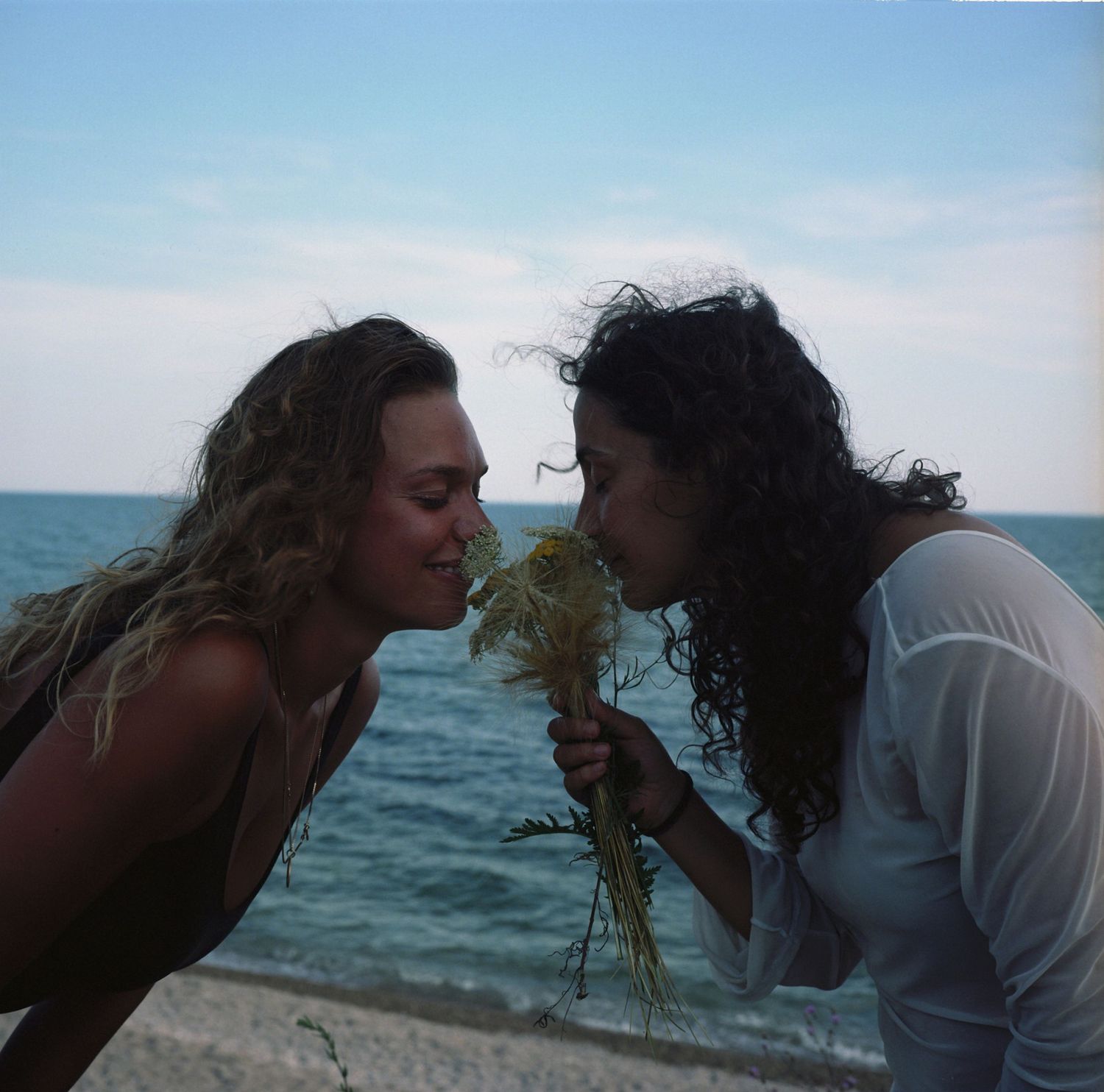 Two people sharing a playful moment at the beach with ocean waves in the background.