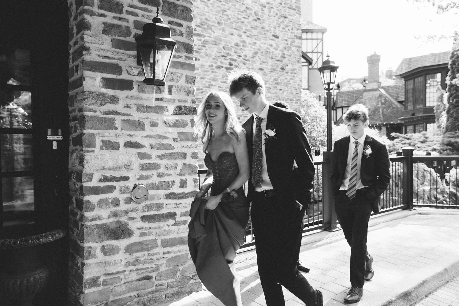 Black and white photo of elegantly dressed wedding guests walking outside a stone building.