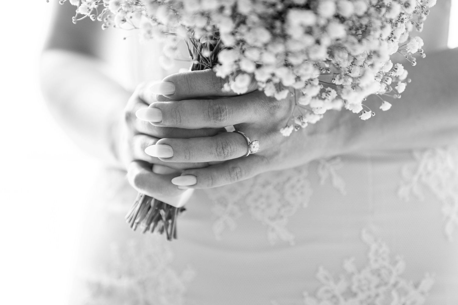 Black and white photo of a bride holding a delicate baby's breath bouquet, wearing a lace wedding dress and ring.
