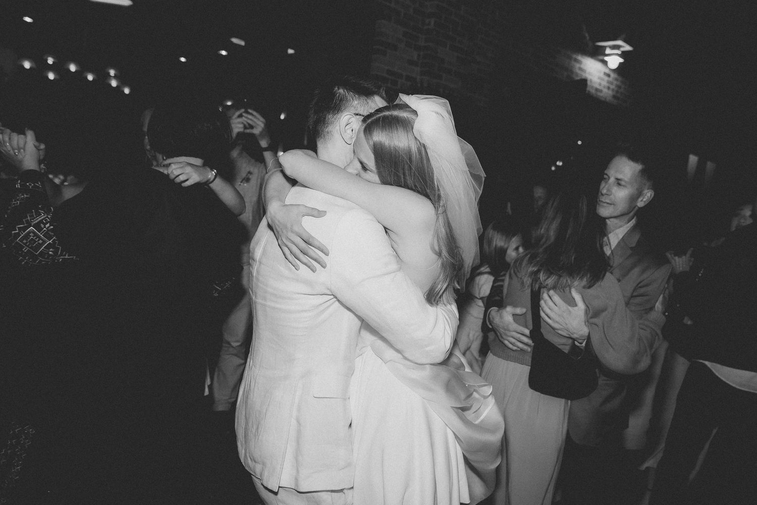Black and white photo of a couple sharing a first dance embrace at a wedding reception.