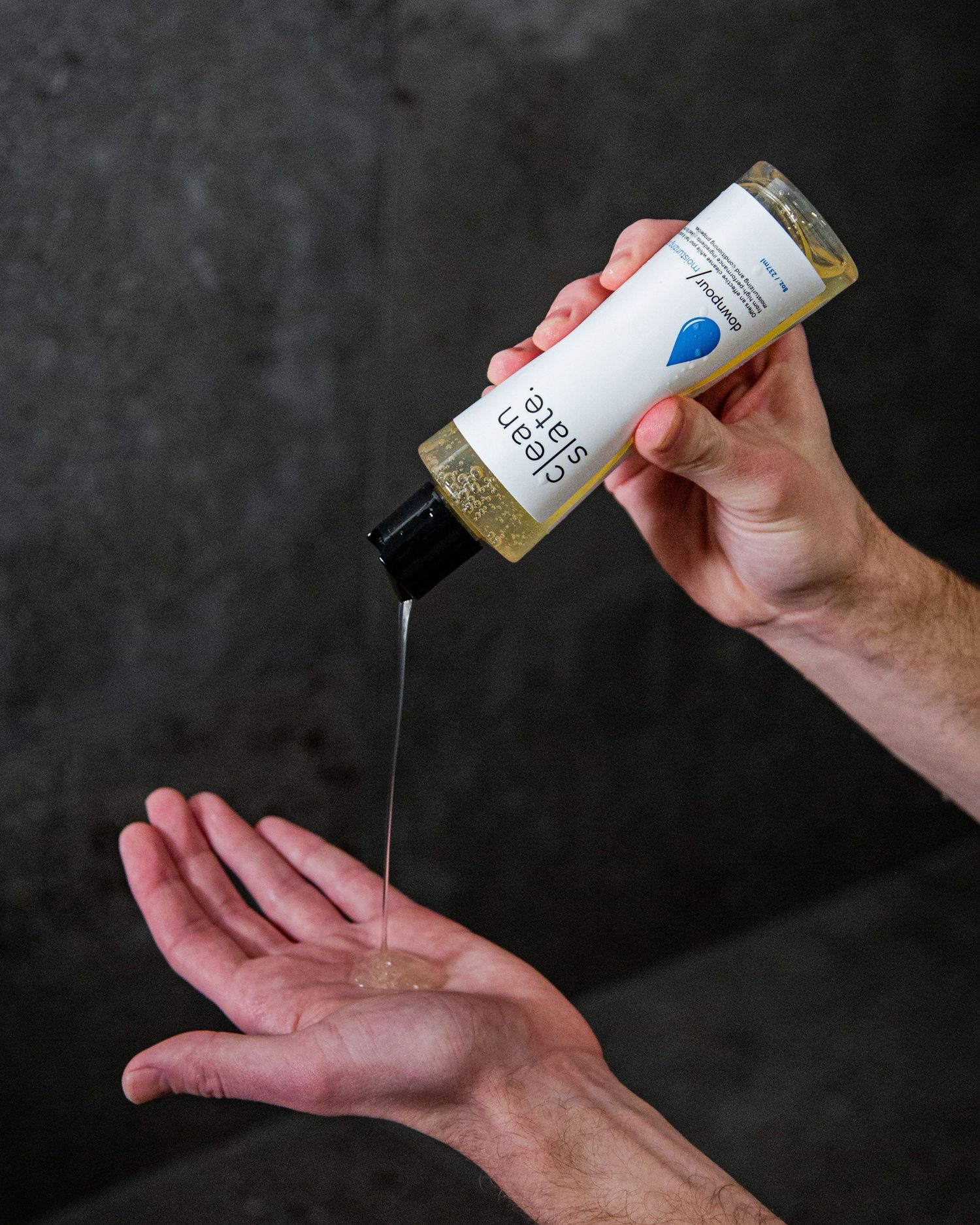 Person dispensing skincare product from clean slate bottle onto hand.