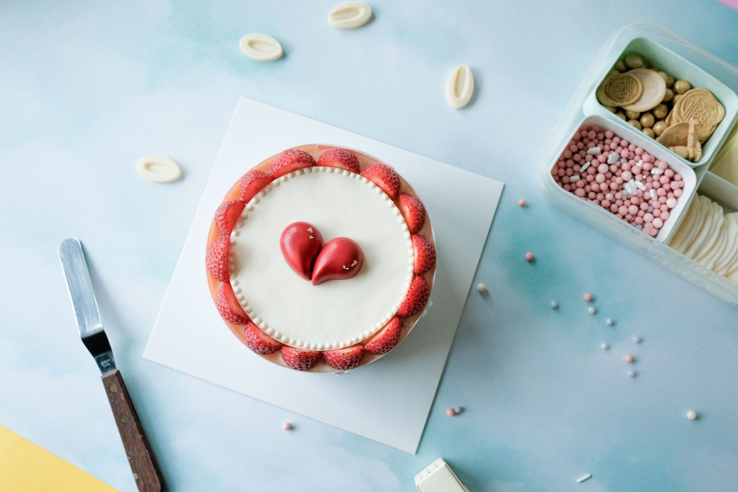 A white cake decorated with fresh strawberries and a red heart design on top against a blue background.