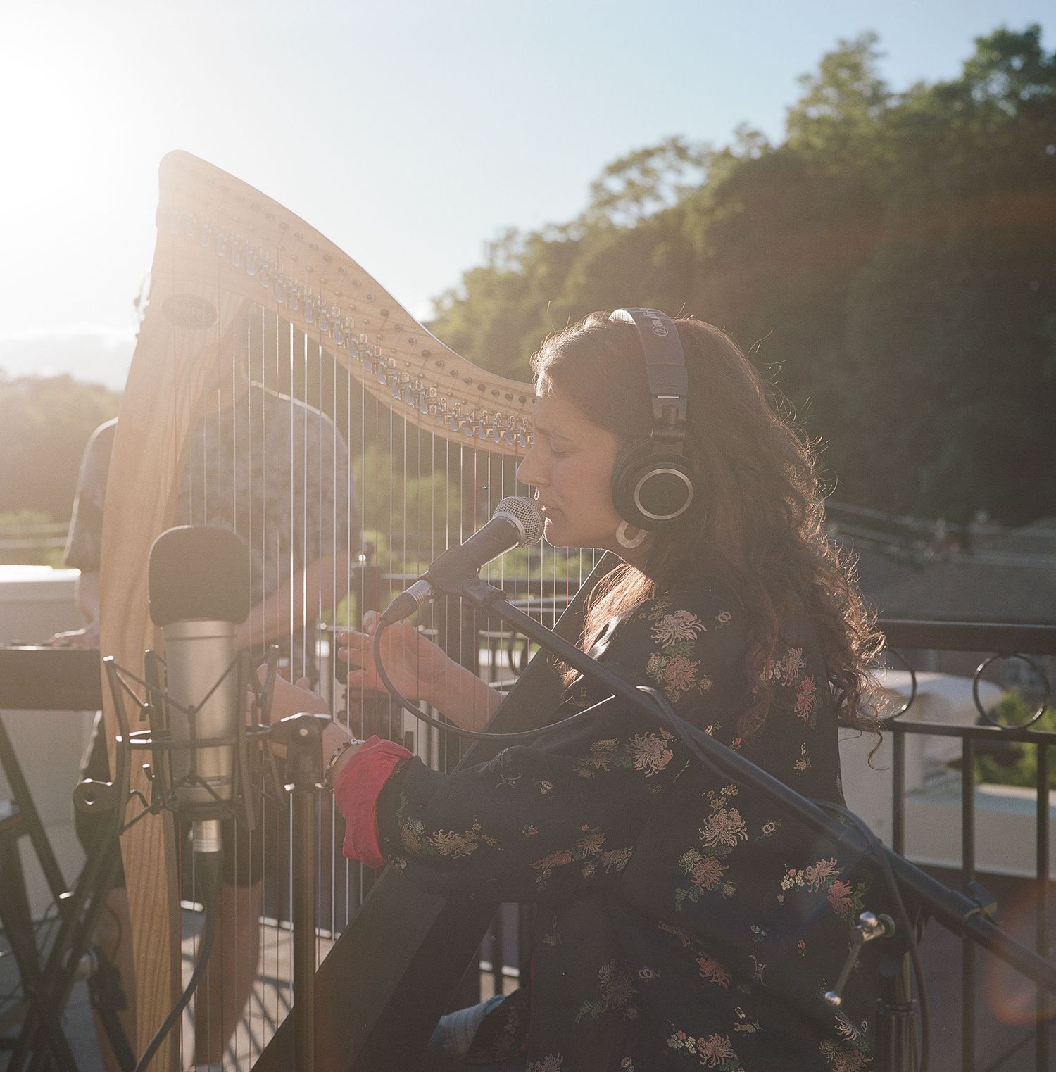 A musician performs on a golden harp outdoors during sunset.