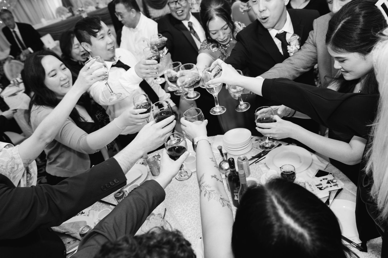 Black and white photo of a group of people raising glasses in a celebratory toast at a formal dinner event.