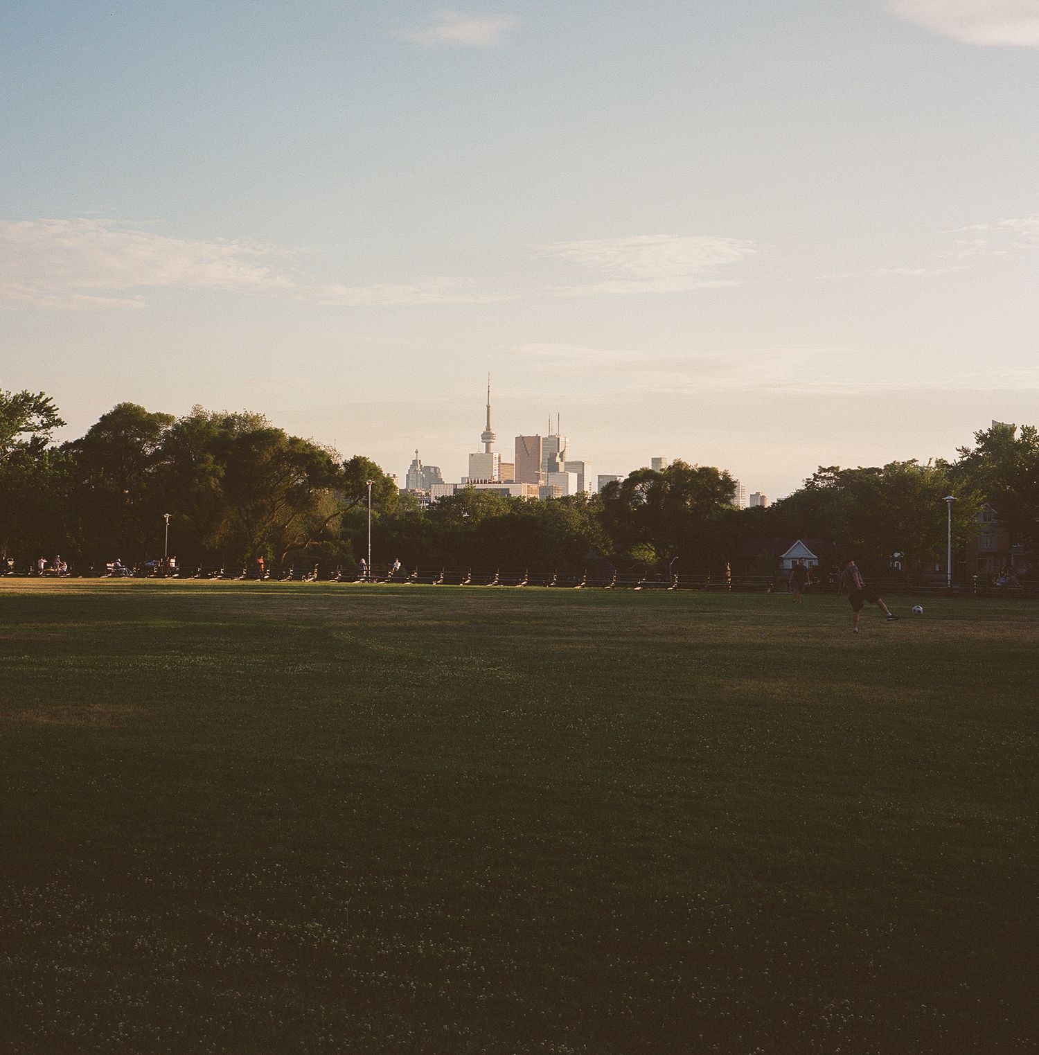 Wide landscape view of open field at sunset with distant buildings.