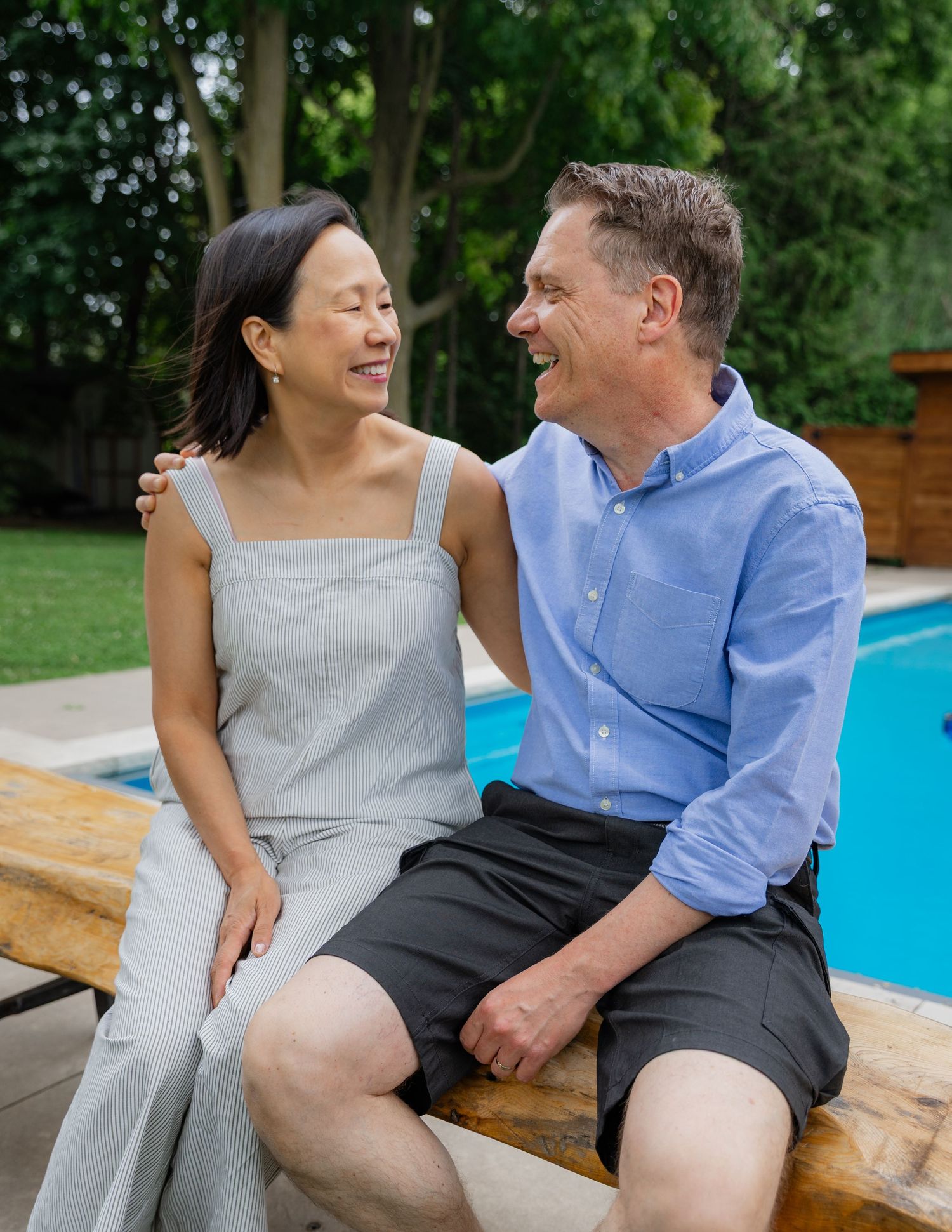 Couple sharing joyful moments while sitting by a blue pool on a summer day.