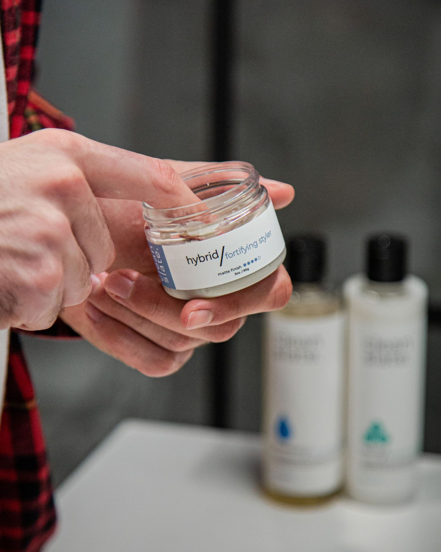 Close-up of hands holding and examining skincare product container in bathroom.