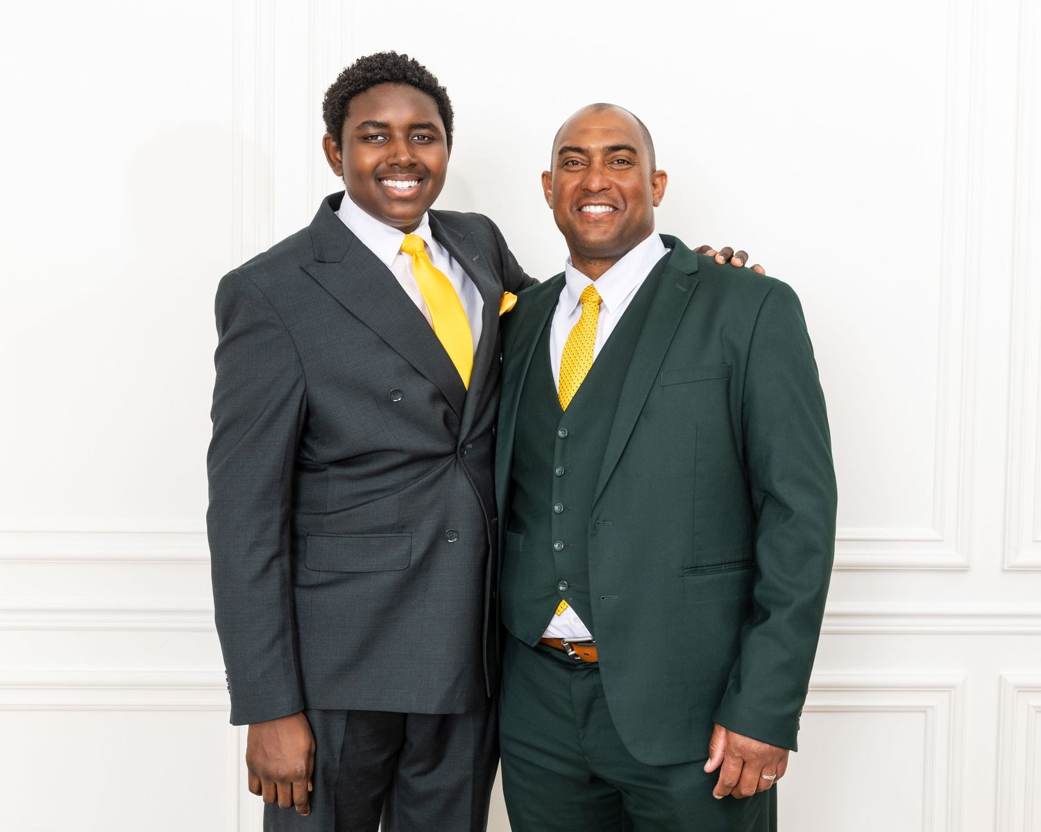 Two people in dark business suits with yellow accents standing together.