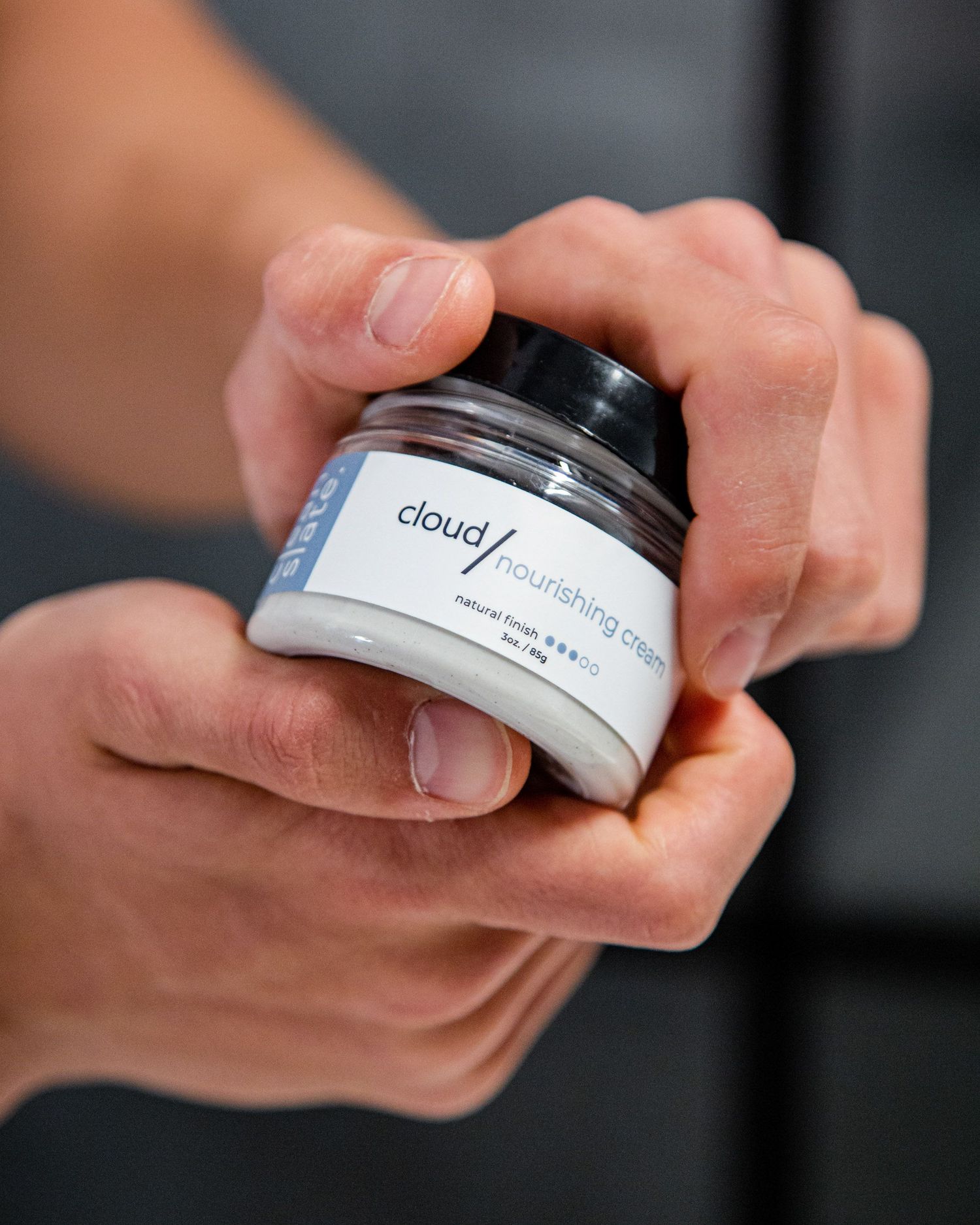 Close-up of hands holding and examining cloud skincare product container.