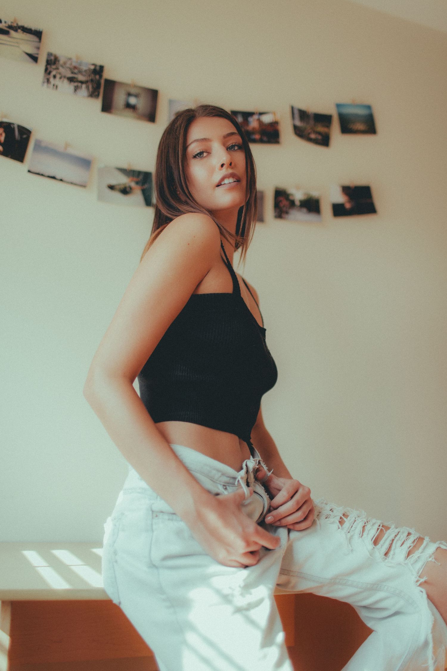 Casual indoor portrait with photos displayed on wall in warm lighting.