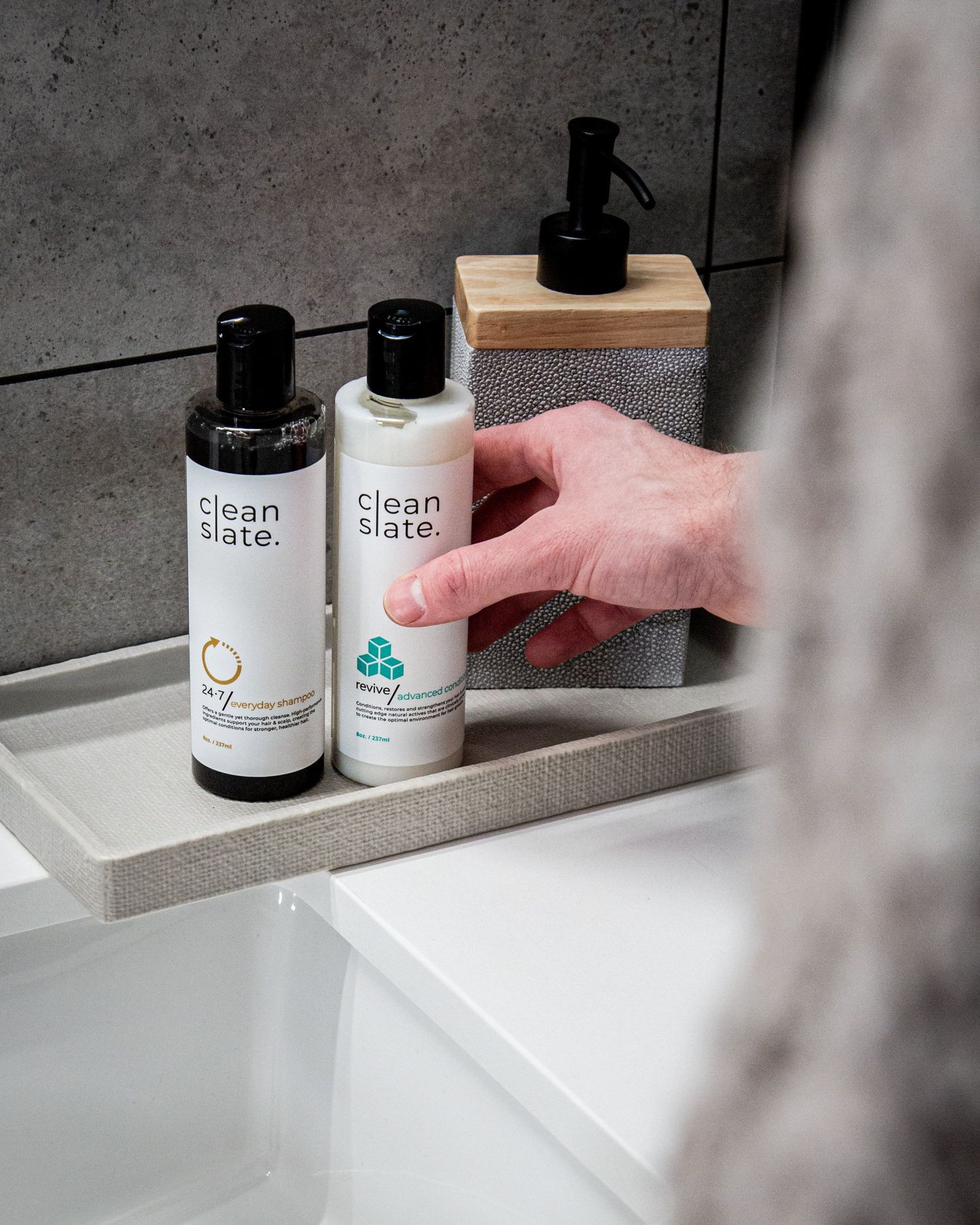 Clean Slate beauty products arranged on a modern gray bathroom shelf with wooden soap dispenser.