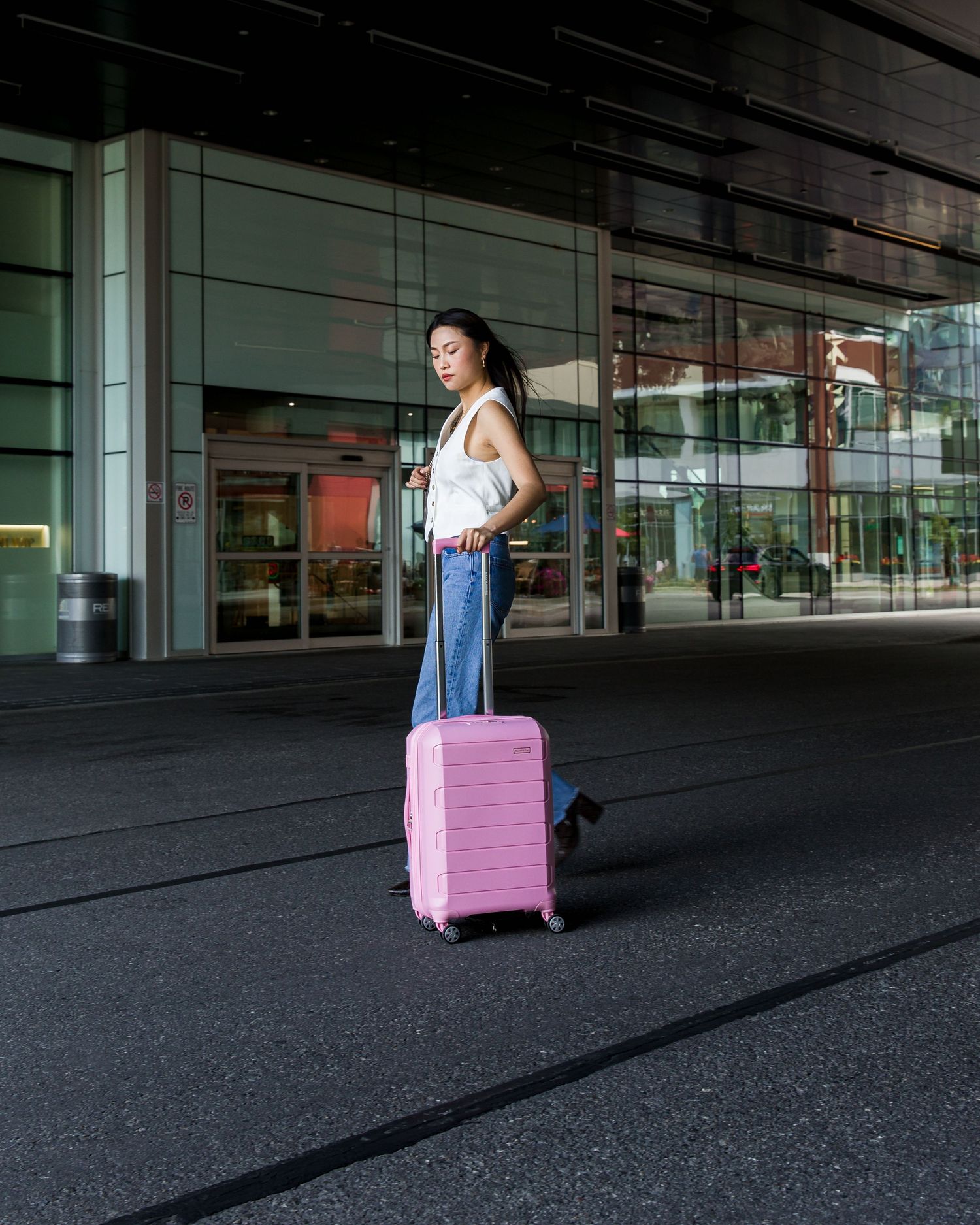 Person pulling pink suitcase through dark urban setting with modern architecture.