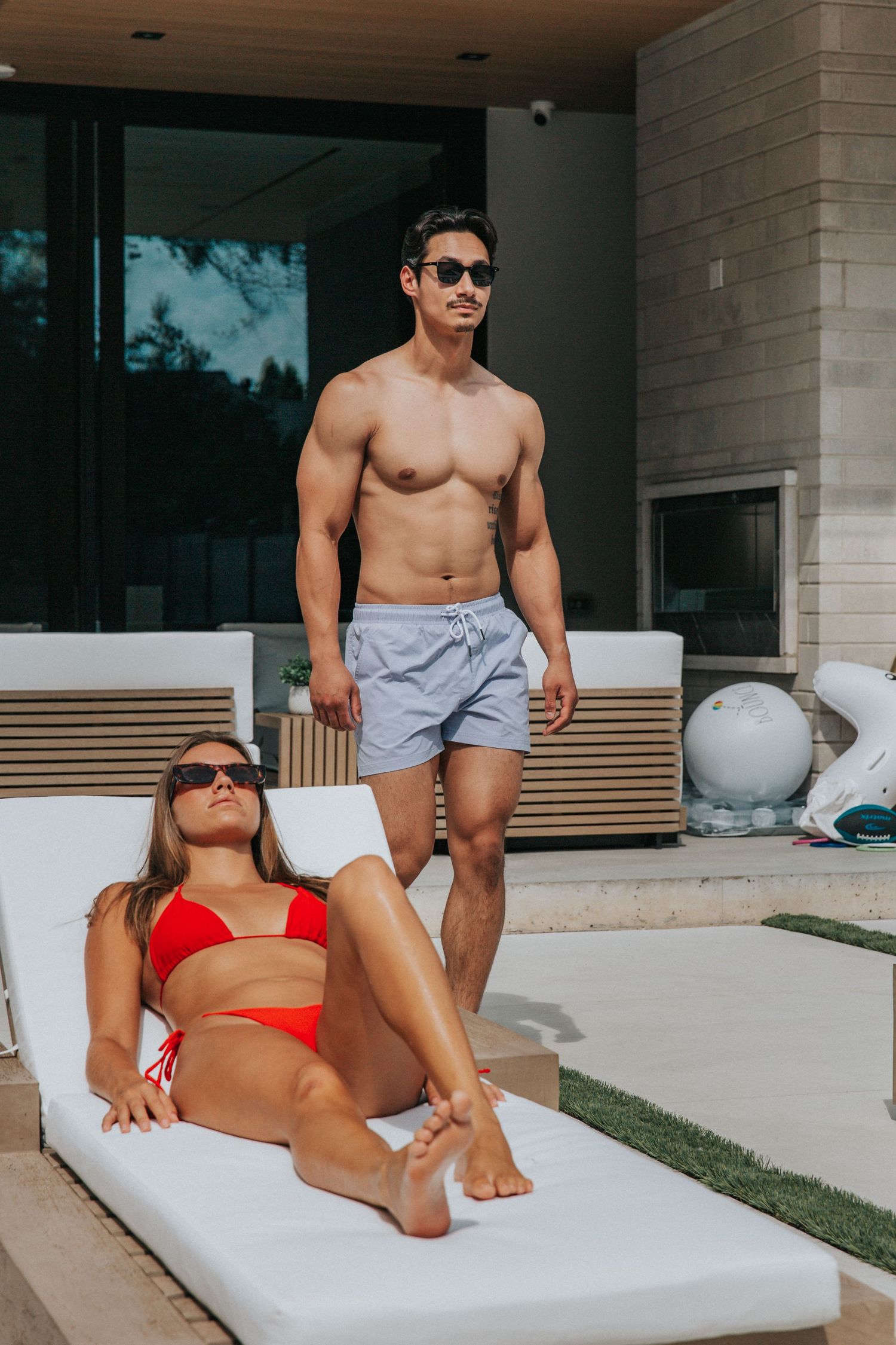 Couple relaxing on outdoor lounge chairs by modern building on sunny day.
