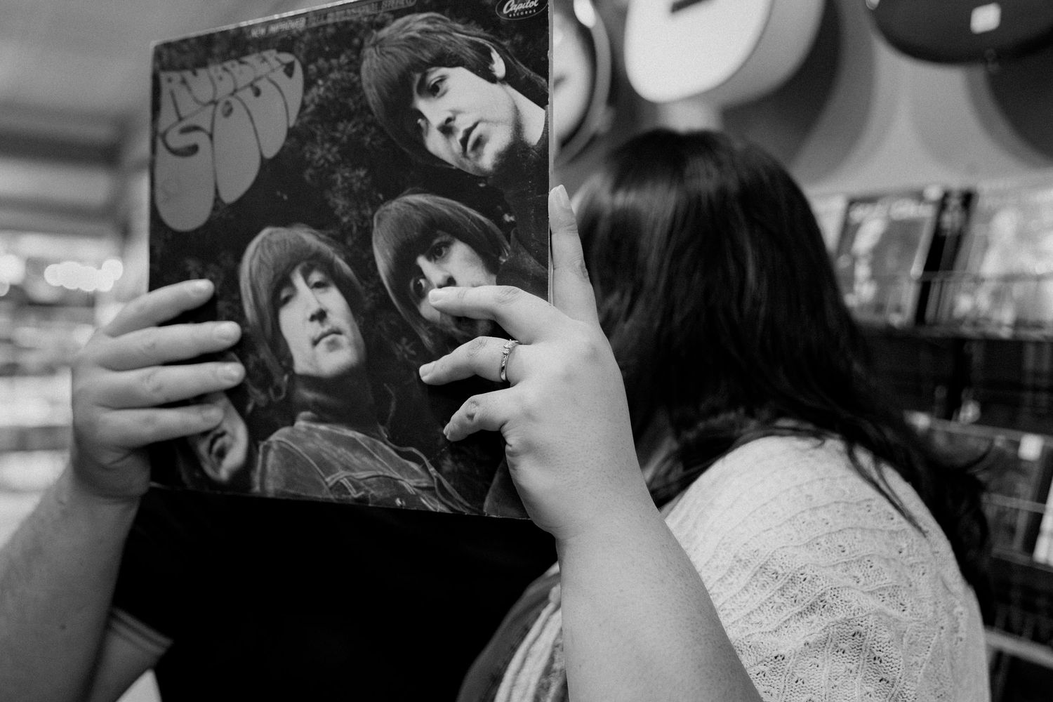 Black and white photo of a person holding a Beatles Rubber Soul vinyl record album in a music store.